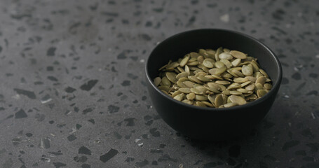 pumpkin seeds in black bowl on terrazzo countertop with copy space