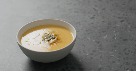 pumpkin cream soup in white bowl on terrazzo countertop with copy space