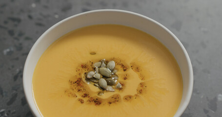 closeup pumpkin cream soup in white bowl on terrazzo countertop