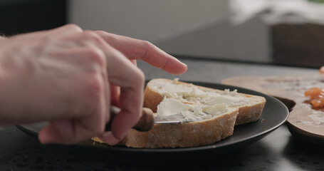 man spread cream cheese on ciabatta slice on black plate