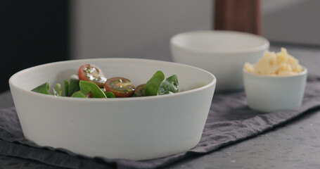 pour olive oil into salad with kumato tomatoes and spinach in white bowl