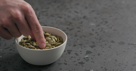 man hand takes pumpkin seeds from white bowl with copy space