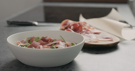 adding prosciutto to make salad with arugula, and tomatoes