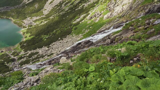 Scenic view of Velicky vodopad (Velicky waterfall) running down towards blue water of Velicke Pleso (Velicke tarn) in Slovakia, High Tatras mountains. Wild flowing water on rocky mountains