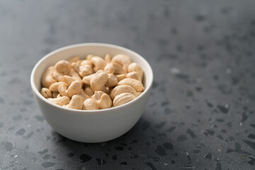 Dry cashew nuts in white bowl on concrete background with copy space