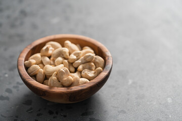 Dry cashew nuts in wood olive bowl on concrete background with copy space
