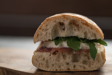 Sandwich with prosciutto, mozzarella and arugula on olive wooden board with copy space