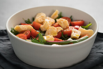 salad with cherry tomatoes, mixed grens and cheese in white bowl on concrete background