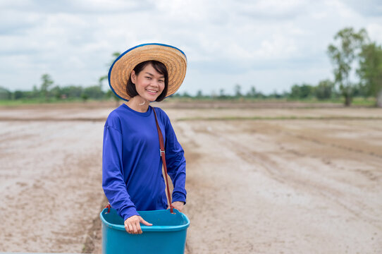 Asian farmer woman holding blue pucket standing and smile at rice farm field