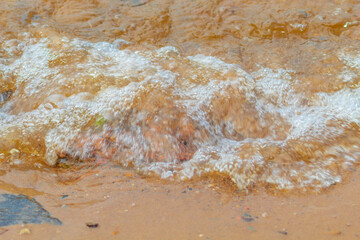 Fototapeta na wymiar River wave with foam washes the sandy bank of the river in the city in the summer