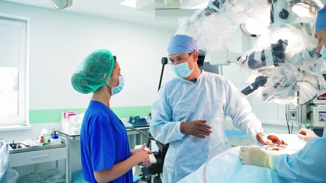 Medical specialists in the hospital. Conversation between doctors in the surgical room. Surgeon and female doctor in medical uniform have a talk during surgery.