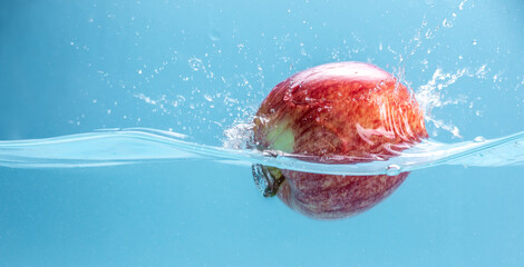 Ripe red apple is falling into clear water, forming lots of splashes. Concept of tasty juicy fruits rich in vitamins