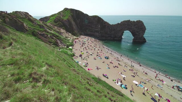 Beautiful landscape of Durdle Door, West Lulworth, Wareham, England. People on Holiday in August 2020 relaxing on the beach with vibrant green nature and rocks in 4K.