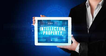 Young business person working on tablet and shows the digital sign: INTELLECTUAL PROPERTY