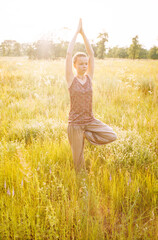Young Caucasian woman doing yoga in a field at summer sunset. Real grain scanned film.