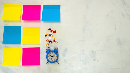 Several blank colorful post-it notes with copy space for text on light background. Blue alarm clock, push pins.  Concept prepare for teamwork or brainstorming. Top view. Flat lay. Close-up.