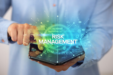 Businessman holding a foldable smartphone with RISK MANAGEMENT inscription, new business concept