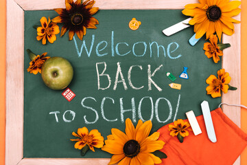 Blackboard with the inscription WELCOME BACK TO SCHOOL,flowers and protective face mask.Back to...