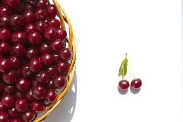 Cherries on a white background. Cherries in a wooden wicker basket on a white background. Two cherries are blurred next to the basket. Top view.