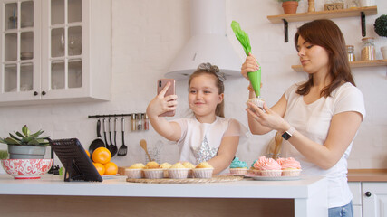 Mother and daughter icing cupcakes and having video call