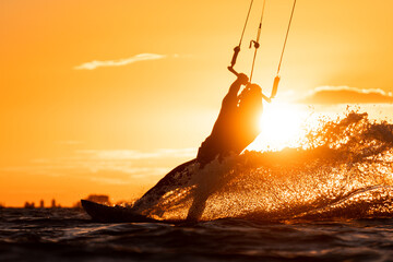 Silhouette of kitesurfer right before take off in beautiful yellow sunset conditions with spray...