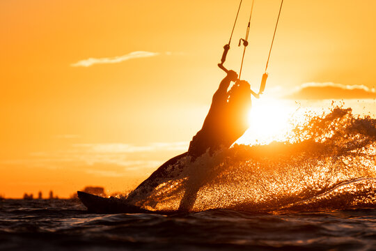 Silhouette of kitesurfer right before take off in beautiful yellow sunset conditions with spray water backlit by the sun