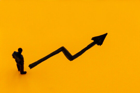 Miniature figurine posed as businessman in front of ascending graph arrow, positive performance concept image