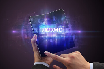 Businessman holding a foldable smartphone with BROADBAND inscription, new technology concept