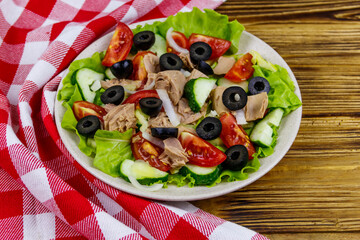 Tasty tuna salad with lettuce, black olives and fresh vegetables on wooden table