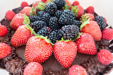 Summer fruits, strawberries, raspberries and blackberries decorate the top of a chocolate cake,
