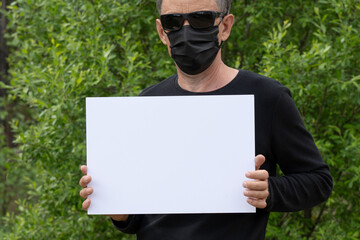 Mockup in the hands of a man. A man in a black medical mask and black glasses on a background of a...