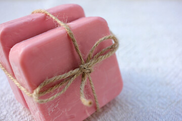 Two bars of pink handmade soap tied with twine on the white wooden background. Selective focus, copy space