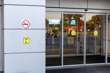 No smoking sign and a sign to call for help for disabled people at the entrance with large glass...