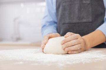 Woman hands kneading dough on board sprinkled with flour on background of light scandi kitchen