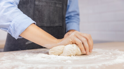 Woman hands kneading dough on wood table background of light scandi kitchen