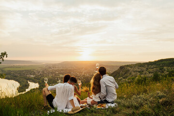 Group of friends sitting on the mountain and enjoying amazing landscape. They have fun during...