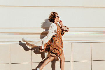 Graceful young woman in long dress running somewhere. Outdoor portrait of active glamorous girl in coat.