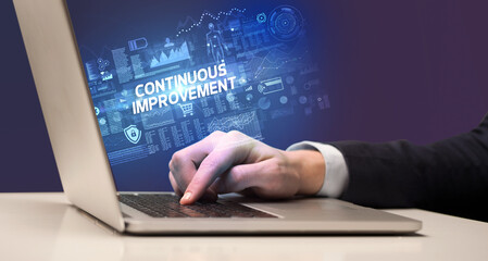 Businessman working on laptop with CONTINUOUS IMPROVEMENT inscription, cyber technology concept
