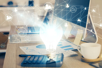 Computer on desktop in office with bulb icon hologram. Multi exposure. Concept of idea.