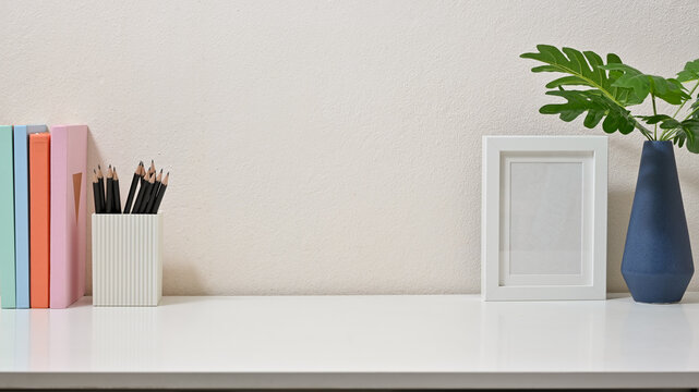Modern decor of workspace with books, pencils, frame and vase on white background. Front view.