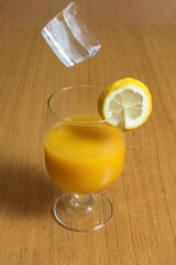 Ice about to fall into a glass full of delicious juice on the kitchen table.