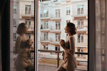 Shapely pleased girl drinking cappuccino and looking at city. Photo of good-humoured lady with cup...