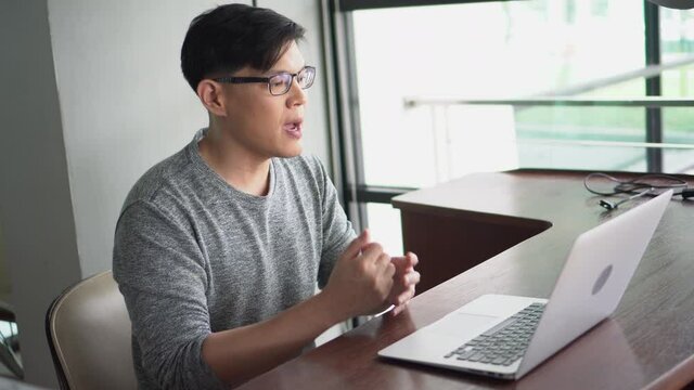 Asian young business man using laptop video conference talking to colleagues meeting online work from home quarantine during Coronavirus pandemic