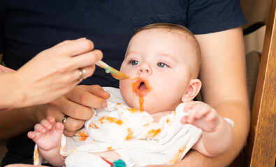Tiny baby boy eating his vegetable carrot meal for the first time. Parents feeding a baby with a spoon - expanding diet.