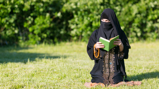 A woman from the East performs morning prayer while. A woman from the East performs morning prayer while sitting in a park green grass.
