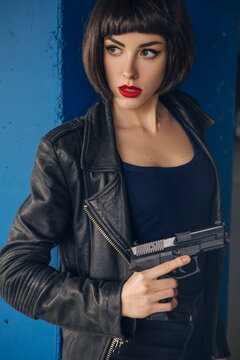 Beautiful brunette sexy spy agent (killer or police) woman in leather jacket and jeans with a gun in her hand running after someone, to catch him on parking