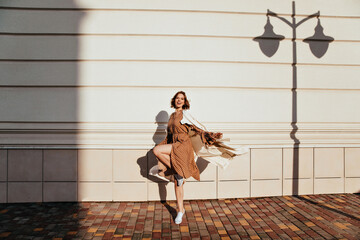 Full-length portrait of active girl dancing in sunny day. Outdoor photo of debonair curly woman fooling around on the street.