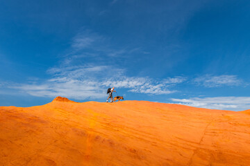 Fototapeta na wymiar Man Walking with Dog on Edge of Red Mountains at Blue Sky