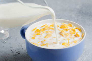 Milk is poured into corn flakes. Blue Cup on a concrete background. Healthy and nutritious Breakfast