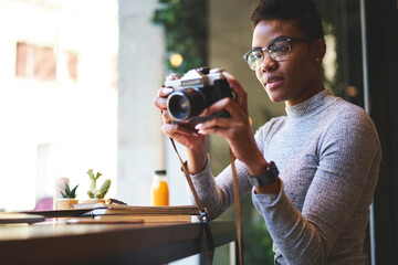 Attractive afro american photographer making pictures of cafe interior earning money using creative ideas,young casually dressed female black model pending time on hobby taking photo on vintage camera